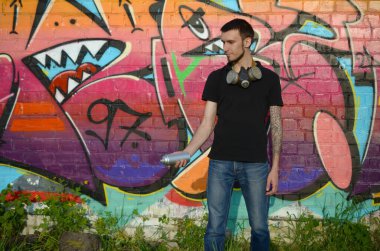 Beyaz beyaz grafiti sanatçısı siyah tişörtlü, sprey sprey boyalı tuğla duvarında renkli pembe grafitilerin yanında. Sokak sanatı ve çağdaş boyama süreci. Gençlik alt kültüründe eğlence