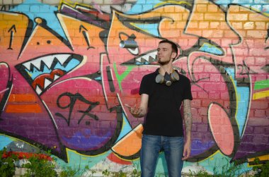 Boynunda gaz maskesi olan genç bir grafiti sanatçısı sprey kutusunu renkli pembe duvar yazısına fırlatıyor. Sokak sanatı ve çağdaş boyama süreci. Gençlik alt kültüründe eğlence