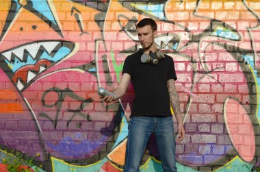 Beyaz beyaz grafiti sanatçısı siyah tişörtlü, sprey sprey boyalı tuğla duvarında renkli pembe grafitilerin yanında. Sokak sanatı ve çağdaş boyama süreci. Gençlik alt kültüründe eğlence