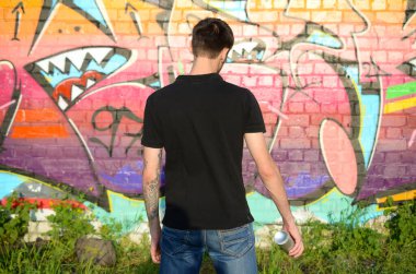Sırt çantası ve gaz maskesi takan genç grafiti sanatçısı, tuğla duvara pembe tonlarda grafiti yapıyor. Sokak sanatı ve çağdaş boyama süreci. Gençlik alt kültüründe eğlence