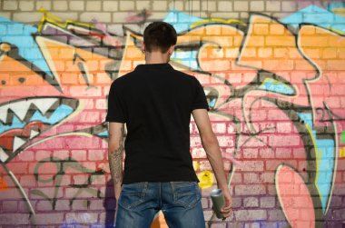 Sırt çantası ve gaz maskesi takan genç grafiti sanatçısı, tuğla duvara pembe tonlarda grafiti yapıyor. Sokak sanatı ve çağdaş boyama süreci. Gençlik alt kültüründe eğlence