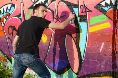 Sırt çantası ve gaz maskesi takan genç grafiti sanatçısı, tuğla duvara pembe tonlarda grafiti yapıyor. Sokak sanatı ve çağdaş boyama süreci. Gençlik alt kültüründe eğlence
