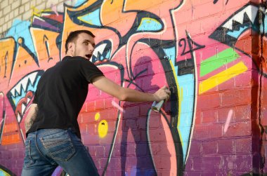 Sırt çantası ve gaz maskesi takan genç grafiti sanatçısı, tuğla duvara pembe tonlarda grafiti yapıyor. Sokak sanatı ve çağdaş boyama süreci. Gençlik alt kültüründe eğlence