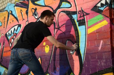 Sırt çantası ve gaz maskesi takan genç grafiti sanatçısı, tuğla duvara pembe tonlarda grafiti yapıyor. Sokak sanatı ve çağdaş boyama süreci. Gençlik alt kültüründe eğlence