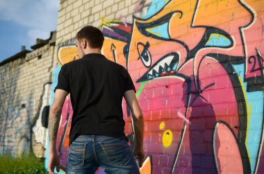 Sırt çantası ve gaz maskesi takan genç grafiti sanatçısı, tuğla duvara pembe tonlarda grafiti yapıyor. Sokak sanatı ve çağdaş boyama süreci. Gençlik alt kültüründe eğlence