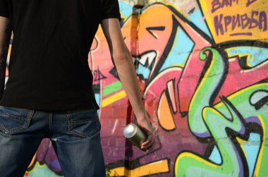 Sırt çantası ve gaz maskesi takan genç grafiti sanatçısı, tuğla duvara pembe tonlarda grafiti yapıyor. Sokak sanatı ve çağdaş boyama süreci. Gençlik alt kültüründe eğlence