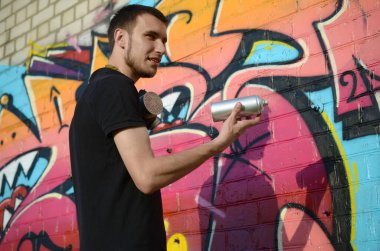 Sırt çantası ve gaz maskesi takan genç grafiti sanatçısı, tuğla duvara pembe tonlarda grafiti yapıyor. Sokak sanatı ve çağdaş boyama süreci. Gençlik alt kültüründe eğlence