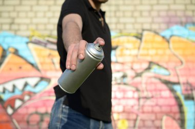 Genç grafiti sanatçısı sprey kutusunu duvardaki pembe tonlarda renkli grafitilerin arka planına doğrultuyor. Sokak sanatı ve çağdaş boyama süreci. Gençlik alt kültüründe eğlence