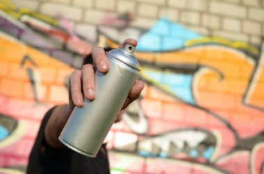 Genç grafiti sanatçısı sprey kutusunu duvardaki pembe tonlarda renkli grafitilerin arka planına doğrultuyor. Sokak sanatı ve çağdaş boyama süreci. Gençlik alt kültüründe eğlence