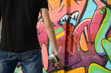 Sırt çantası ve gaz maskesi takan genç grafiti sanatçısı, tuğla duvara pembe tonlarda grafiti yapıyor. Sokak sanatı ve çağdaş boyama süreci. Gençlik alt kültüründe eğlence