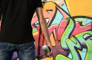 Sırt çantası ve gaz maskesi takan genç grafiti sanatçısı, tuğla duvara pembe tonlarda grafiti yapıyor. Sokak sanatı ve çağdaş boyama süreci. Gençlik alt kültüründe eğlence