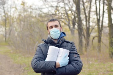 Covidiot konsepti. Koruyucu maskeli genç adam, yay ağacında bir sürü tuvalet kağıdı tutuyor. Karantina sırasında panik satın alma