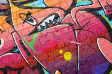 Eski tuğla duvardaki graffiti resimlerinin soyut renkli bir parçası. Vahşi harfler ve renkli lekelerle dolu sokak sanatı kompozisyonu. Sıcak renklerde alt kültür arkaplan dokusu