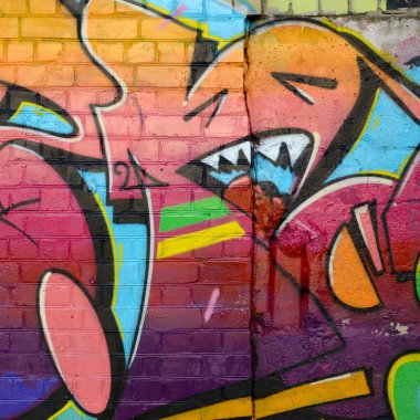 Eski tuğla duvardaki graffiti resimlerinin soyut renkli bir parçası. Vahşi harfler ve renkli lekelerle dolu sokak sanatı kompozisyonu. Sıcak renklerde alt kültür arkaplan dokusu