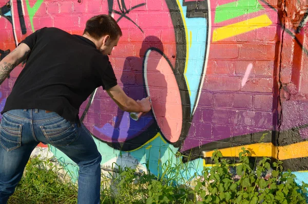 Young Graffiti Artist With Backpack And Gas Mask On His Neck Paints Colorful Graffiti In Pink Tones On Brick Wall Street Art And Contemporary Painting Process Entertainment In Youth Subculture Stock