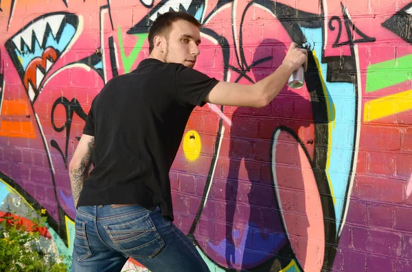 Young Graffiti Artist With Backpack And Gas Mask On His Neck Paints Colorful Graffiti In Pink Tones On Brick Wall Street Art And Contemporary Painting Process Entertainment In Youth Subculture Stock