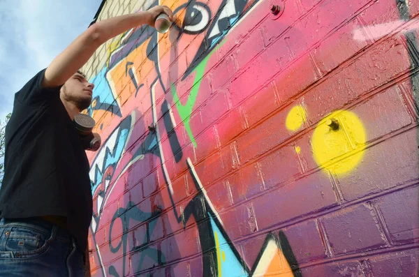 年轻的涂鸦画家 脖子上戴着背包和防毒面具 用粉红的色调在砖墙上画着五彩斑斓的涂鸦 街头艺术和当代绘画过程 青少年亚文化中的娱乐 — 图库照片