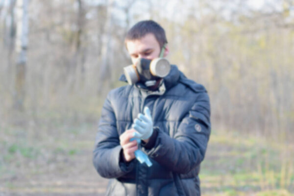 Blurred portrait of young man in protective gas mask wears rubber disposable gloves outdoors in spring wood. Concept of protective goods usage during quarantine