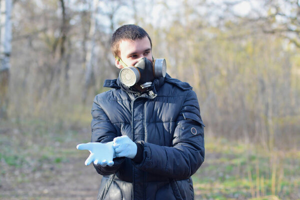 Portrait of young man in protective gas mask wears rubber disposable gloves outdoors in spring wood. Concept of protective goods usage during quarantine