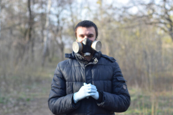 Blurred portrait of young man in protective gas mask wears rubber disposable gloves outdoors in spring wood. Concept of protective goods usage during quarantine
