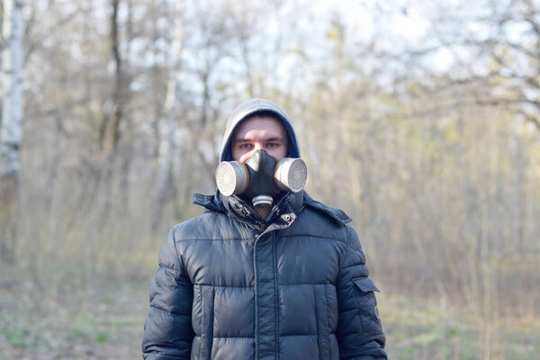 Portrait of young man in protective gas mask outdoors in spring wood. Concept of protective goods usage during quarantine