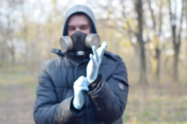 Blurred portrait of young man in protective gas mask wears rubber disposable gloves outdoors in spring wood. Concept of protective goods usage during quarantine