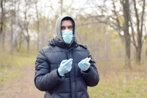 Młody Mężczyzna Masce Ochronnej Pokazuje Butelki Środkiem Dezynfekującym Zewnątrz Wiosennym — Zdjęcie stockowe