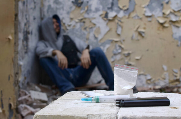 A drug-dependent man suffers from drug withdrawal while sitting in abandoned building next to dose for narcotic injections. Drug adiction problems concept