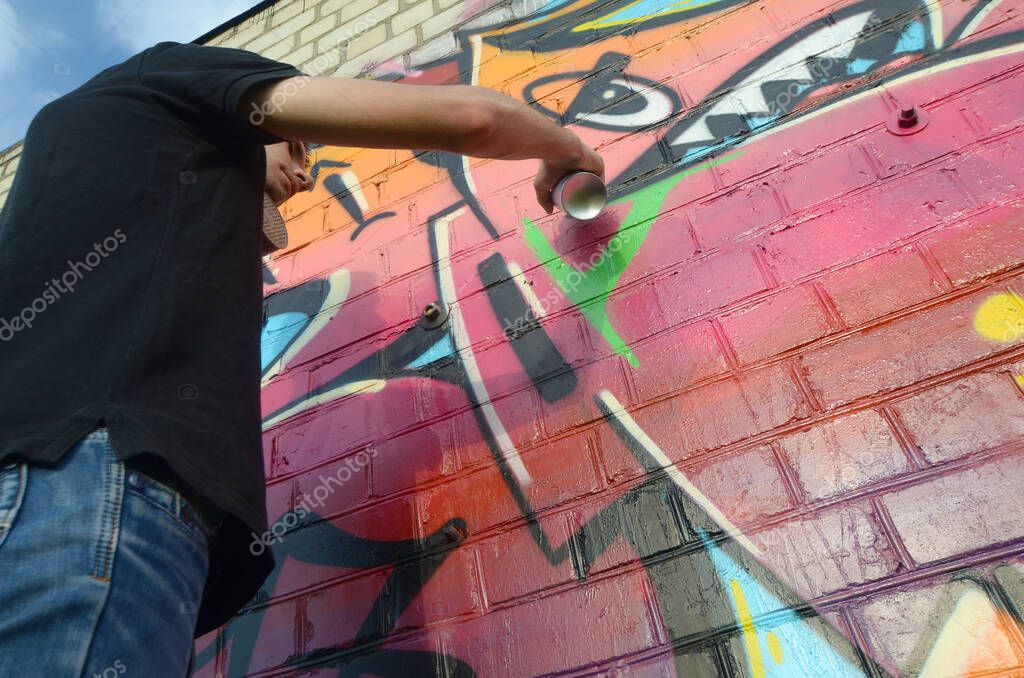 Young Graffiti Artist With Backpack And Gas Mask On His Neck Paints Colorful Graffiti In Pink Tones On Brick Wall Street Art And Contemporary Painting Process Entertainment In Youth Subculture Larastock