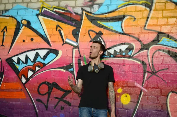 Young Graffiti Artist With Gas Mask On His Neck Throw His Spray Can Against Colorful Pink Graffiti On Brick Wall Street Art And Contemporary Painting Process Entertainment In Youth Subculture Dirty