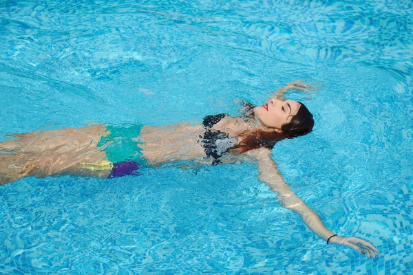 Mooie jonge vrouw in water bij het zwembad ontspannen — Stockfoto
