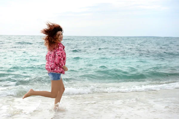 Schöne Mädchen mit bunten Windjacke läuft am Strand — Stockfoto