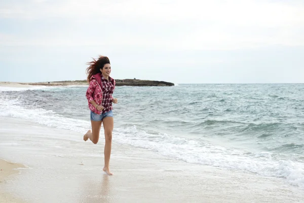 Menina bonita com blusão colorido correndo na praia — Fotografia de Stock