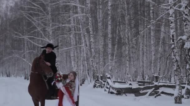 Bruden och brudgummen står i skogen på vintern. Stående bredvid en häst. — Stockvideo