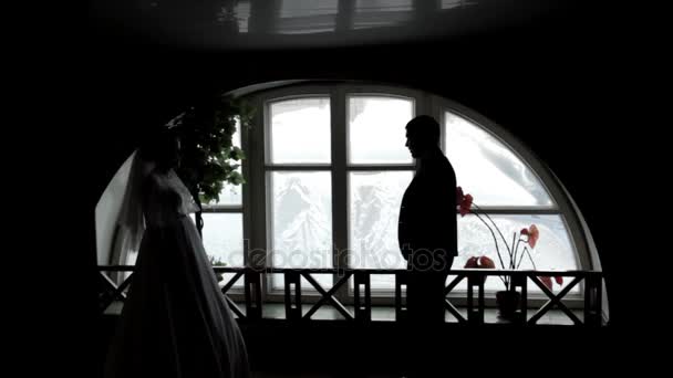 Le marié et la mariée se tiennent à la fenêtre. Des silhouettes de gens. Image en noir et blanc . — Video