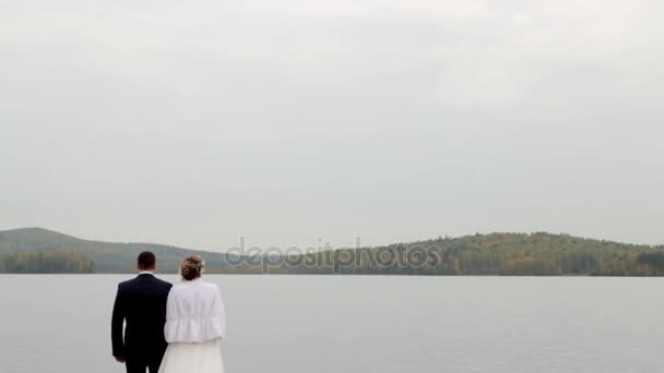Наречений і наречений ходять біля озера, тримаючись за руки. Осінь . — стокове відео