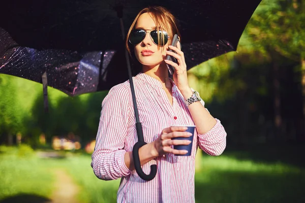 Frau telefoniert auf der Straße unter einem Regenschirm — Stockfoto