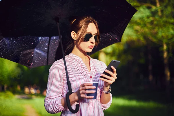 Donna che parla su uno smartphone sotto un ombrello per strada — Foto Stock