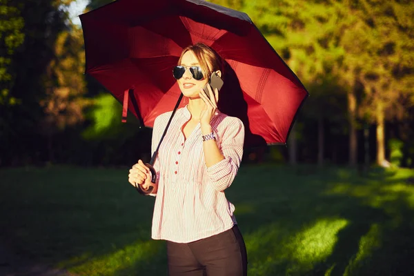 Frau telefoniert auf der Straße unter einem Regenschirm — Stockfoto