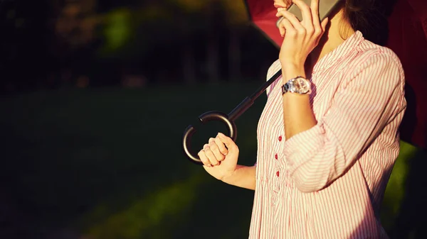 Žena mluvila na chytrý telefon pod slunečníkem na ulici — Stock fotografie