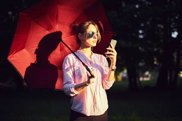 Donna che parla su uno smartphone sotto un ombrello per strada — Foto Stock