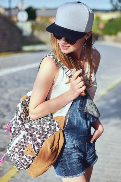 Ragazza con zaino in giro per la città in buona giornata. Ritratto all'aperto di viaggiatore femminile sorridente in cappello in posa con bella architettura sullo sfondo — Foto Stock