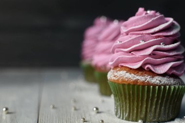 Yeşil kağıt pembe krema ile cupcakes pudra şekeri ve ahşap masa lambası üzerinde gümüş boncuk ile serpilir
