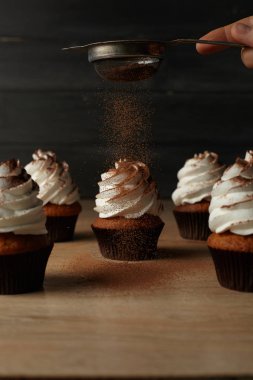 Üzerinde koyu bir arka plan ile ahşap bir masa üzerine kakao tozu dökülür beyaz krema ile cupcakes