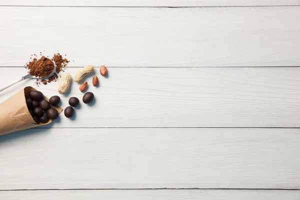 Sweets with peanuts and peanuts with a spoon of cocoa powder on a white wooden background