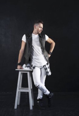 Bir adam bir yelek ve beyaz bir T-shirt ve kot yaslanmış bir sandalye siyah bir arka plan üzerinde poz