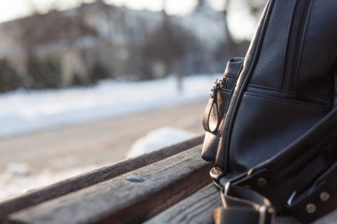 bir ahşap Bank güneşte karlı üzerinde deri sırt çantası siyah 