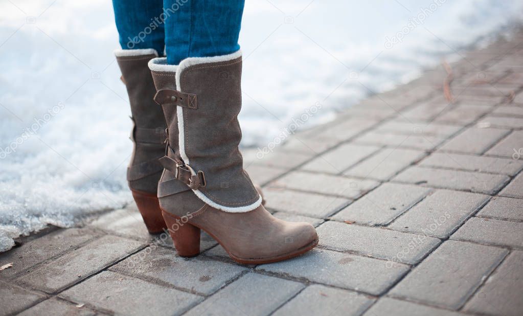 Gray boots with heels with white fur and buckles on paving stones with snow