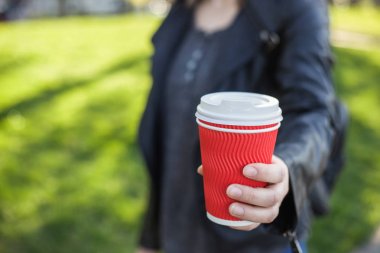 Bir beyaz kapak ve yeşil çim çerçevede bir sokakta bir kızın elinde kahve ile kağıt kırmızı cam
