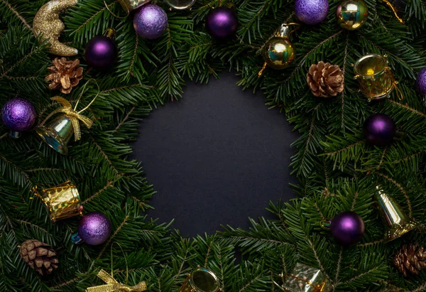 Christmas wreath decorated with purple and gold toys with a black background in the middle